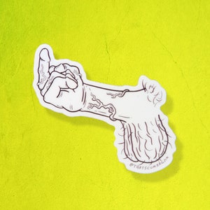 以下が含まれることがあります： 毛むくじゃらの腕と毛むくじゃらのボールがついた、中指を立てている手の白黒線画。絵は「@THATSCUMBAGJIM」という文字が書かれた白いステッカーの上に描かれている。