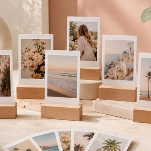 May include: A collection of six rectangular photo prints with white borders, each displayed in a small, light-coloured wooden block stand. The prints feature various scenes including a narrow street, flowers, a beach, a person, buildings, and palm trees.