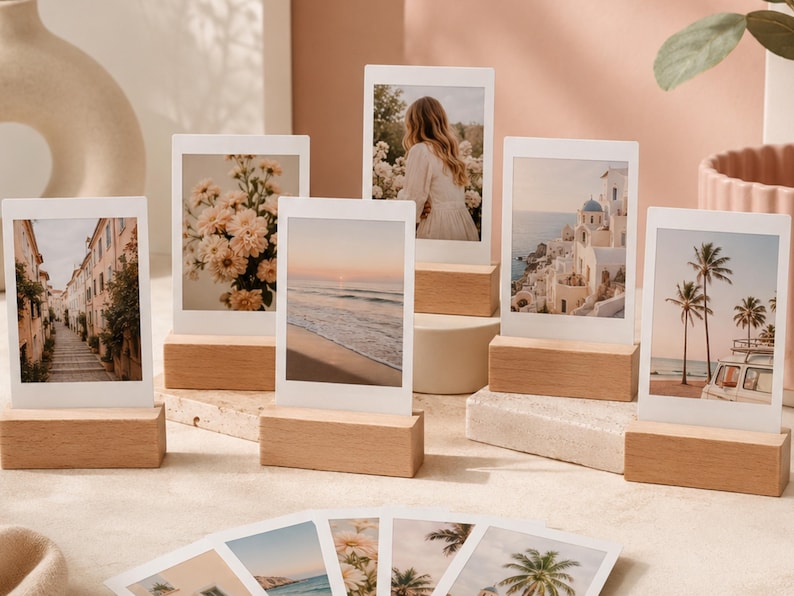 May include: A collection of six rectangular photo prints with white borders, each displayed in a small, light-coloured wooden block stand. The prints feature various scenes including a narrow street, flowers, a beach, a person, buildings, and palm trees.