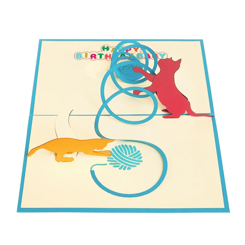 Op de afbeelding: Pop-up verjaardagskaart met twee katten die met een blauwe bol wol spelen. E&eacute;n kat is oranje, de andere rood. De kaart heeft een blauwe rand en de tekst "HAPPY BIRTHAY" in regenboogkleuren.