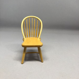 May include: A wooden chair with a spindle back and a light brown finish. The chair has a simple design with four legs and a curved back.