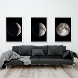 May include: Three black and white framed photographs of the moon in different phases hanging on a white wall above a black leather sofa with a gray throw blanket.