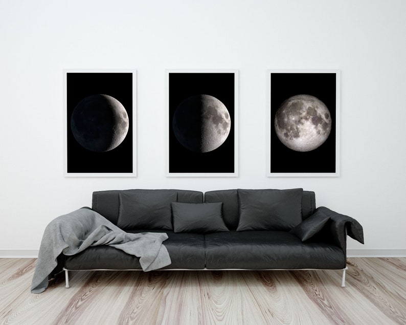 May include: Three black and white framed photographs of the moon in different phases hanging on a white wall above a black leather sofa with a gray throw blanket.
