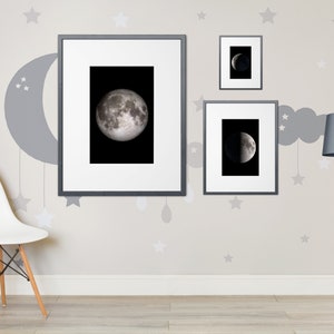 May include: Three framed black and white photographs of the moon in different phases hanging on a light gray wall with a gray crescent moon and stars painted on the wall. A white chair with wooden legs sits in front of the wall. A black floor lamp with a gray lampshade is on the right side of the wall.