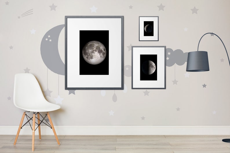 May include: Three framed black and white photographs of the moon in different phases hanging on a light gray wall with a gray crescent moon and stars painted on the wall. A white chair with wooden legs sits in front of the wall. A black floor lamp with a gray lampshade is on the right side of the wall.