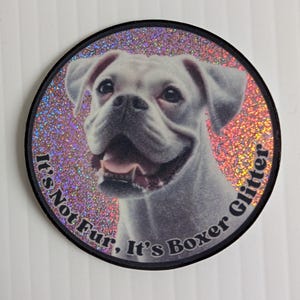 May include: A circular sticker with a smiling white Boxer dog against a glittery backdrop. The text "It's Not Fur, It's Boxer Glitter" is printed in black around the edge, with a black border.