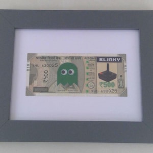 May include: A framed 500 rupee note with a green Pac-Man character and a black joystick with the word "BLINKY" printed on it.