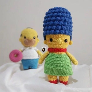 Puede incluir: Juguetes de peluche tejidos a crochet de Bart y Lisa Simpson del programa de televisión animado Los Simpson. Bart sostiene una dona rosa. Lisa lleva una peluca azul, un lazo rojo y un vestido verde.