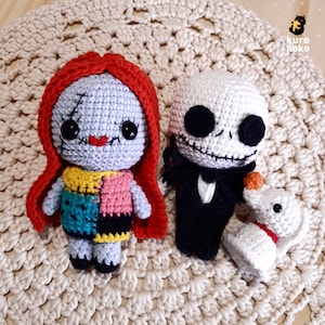 Puede incluir: Muñecas amigurumi de crochet de Sally y Jack Skellington de Pesadilla Antes de Navidad. Sally lleva un vestido de retazos y una capa roja. Jack lleva un traje negro y una pajarita blanca.