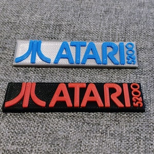 May include: Two rectangular plastic plaques with the Atari logo and the text "5200" printed on them. The top plaque is silver with blue text and the bottom plaque is black with red text.