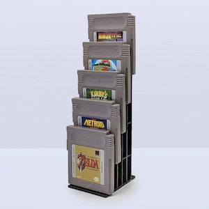 May include: A gray plastic stand with six slots for holding Game Boy cartridges. The cartridges are labeled with the titles "Ninja Gaiden", "Super Mario World 2", "Kirby's Dream Land", "Metroid", and "The Legend of Zelda: A Link to the Past".
