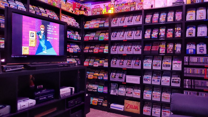 May include: A large collection of video game cartridges organized on shelves. The cartridges are in various colors and are arranged in rows. A television screen is in the foreground, displaying a video game.