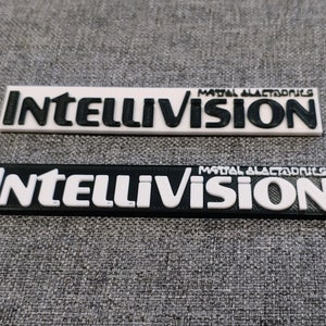 May include: Two black and white plastic plaques with the text "Intellivision" and "Mattel Electronics" printed on them.