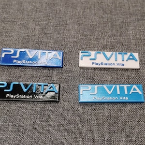 May include: Four different colored plastic stickers with the text "PSVITA PlayStation Vita" in white lettering.
