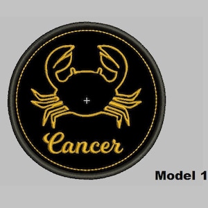 Puede incluir: Un parche bordado negro y dorado con un diseño de cangrejo y la palabra "Cáncer" en letras doradas. El parche es circular y tiene un borde negro.