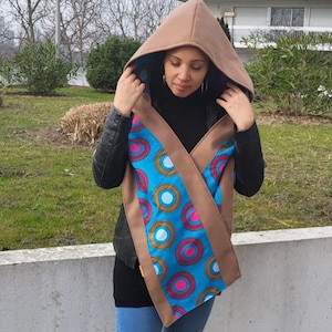 May include: A brown hooded scarf with a blue and white patterned lining. The scarf is worn over a black shirt and blue jeans.