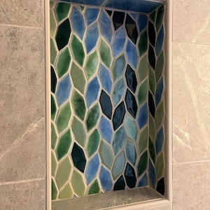 May include: A tiled shower niche with a geometric pattern of blue, green, and black diamond-shaped tiles.