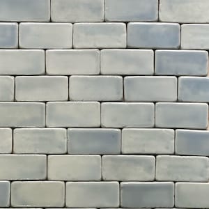 May include: A wall tiled with light blue and white rectangular ceramic tiles. The tiles are arranged in a staggered pattern.