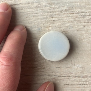 May include: A small, round, white ceramic tile with a light blue glaze.
