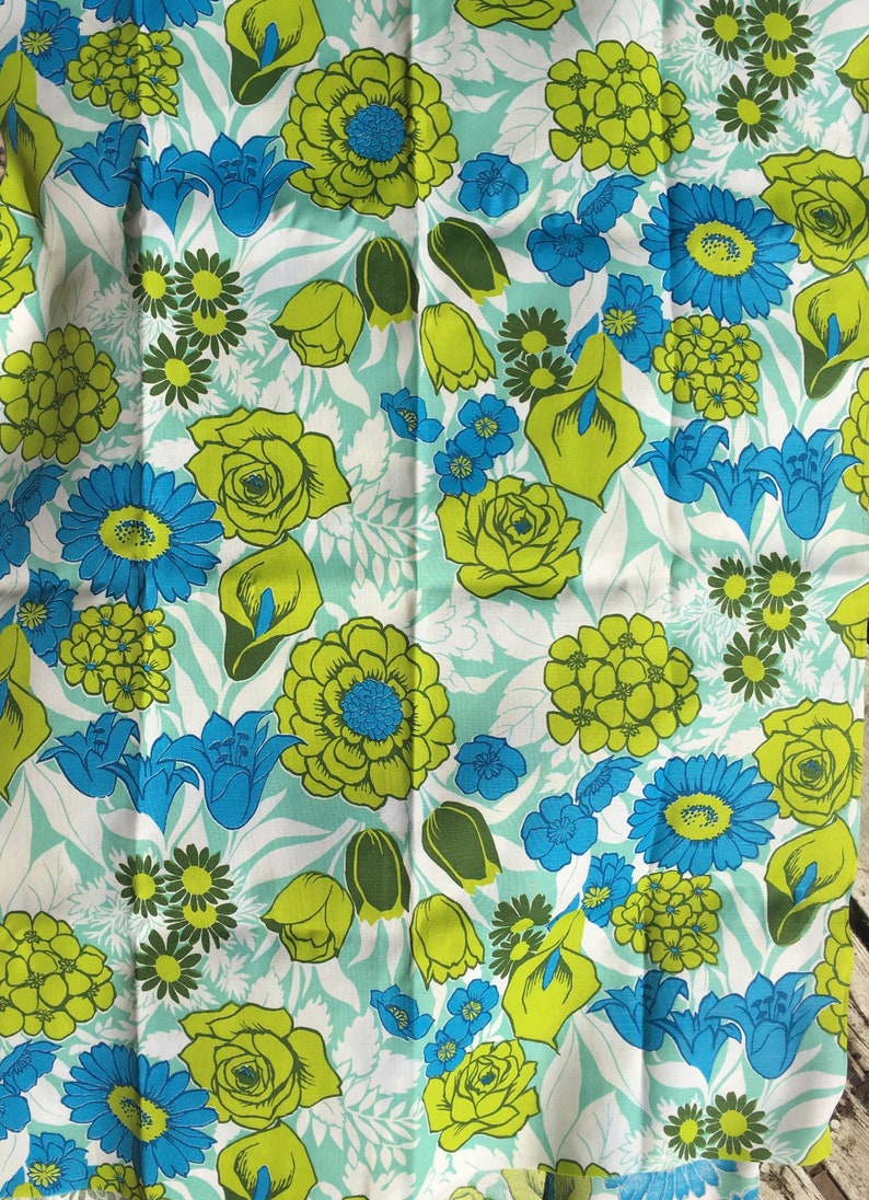 May include: A blue and green floral fabric with a repeating pattern of flowers, leaves, and buds. The fabric has a light blue background with green and blue flowers.