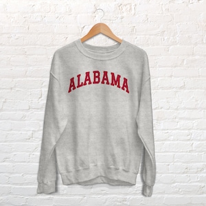 K&ouml;nnte beinhalten: Ein grauer Pullover mit dem Wort "ALABAMA" in Rot auf der Vorderseite.