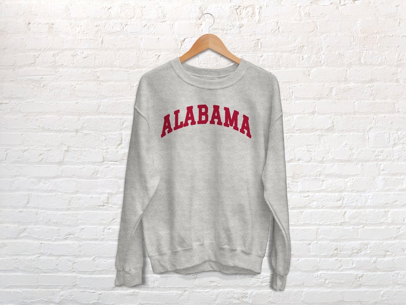K&ouml;nnte beinhalten: Ein grauer Pullover mit dem Wort "ALABAMA" in Rot auf der Vorderseite.