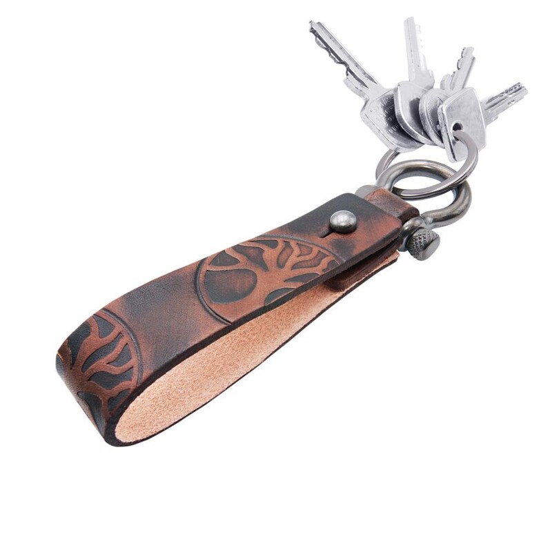 May include: A brown leather keychain with a tree design and a silver metal key ring. The keychain is attached to a set of keys.