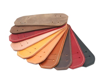 Op de afbeelding: Een selectie van leren riemen in verschillende kleuren, waaronder bruin, rood, oranje, geel en zwart. De riemen zijn in een waaier vorm gerangschikt en hebben een gestikte rand.