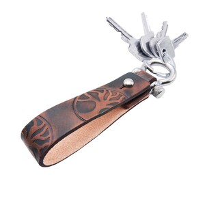 May include: A brown leather keychain with a tree design and a silver key ring. The keychain is made of distressed leather and has a natural, rustic look.