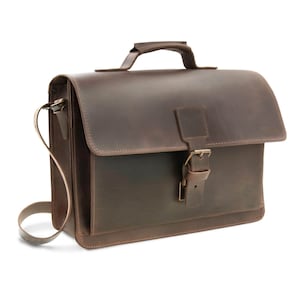 Könnte beinhalten: Eine braune Ledertasche mit einem oberen Griff und einem Schultergurt. Die Tasche hat einen Klappenverschluss mit einer Schnalle und einen kleinen Griff oben. Das Leder hat einen Used-Look.