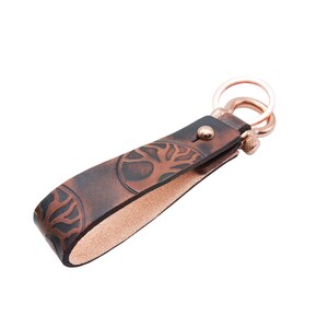 May include: A brown leather keychain with a tree of life design and a rose gold key ring.