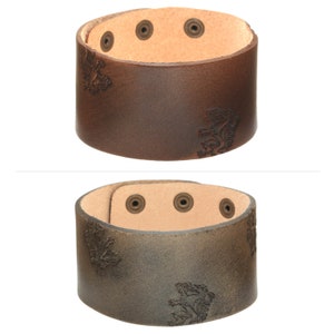 May include: Two leather bracelets with a distressed look. Both bracelets have four metal studs and an embossed lion design.