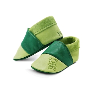 Könnte beinhalten: Ein Paar grüne Lederschuhe für Babys mit einem Teddybär-Motiv. Die Schuhe sind aus weichem, geschmeidigem Leder gefertigt und bieten eine bequeme Passform.