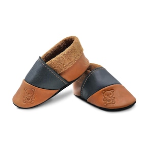 Könnte beinhalten: Ein Paar braune und blaue Lederschuhe für Babys mit einem Teddybär-Design. Die Schuhe haben ein weiches, Wildlederfutter und eine flexible Sohle.