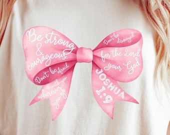 May include: A pink watercolor bow with the text "Be strong & courageous. Don't be afraid. Don't be discouraged for the Lord your God. Joshua 1:9" on a white t-shirt.