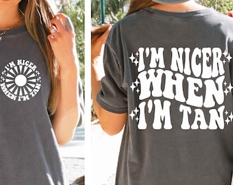 May include: A dark gray t-shirt with a white graphic that says "I'm nicer when I'm tan" in a retro font with stars around the text.