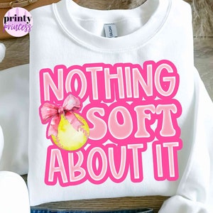 May include: White sweatshirt with pink lettering that says "Nothing Soft About It" with a pink bow and yellow softball graphic.