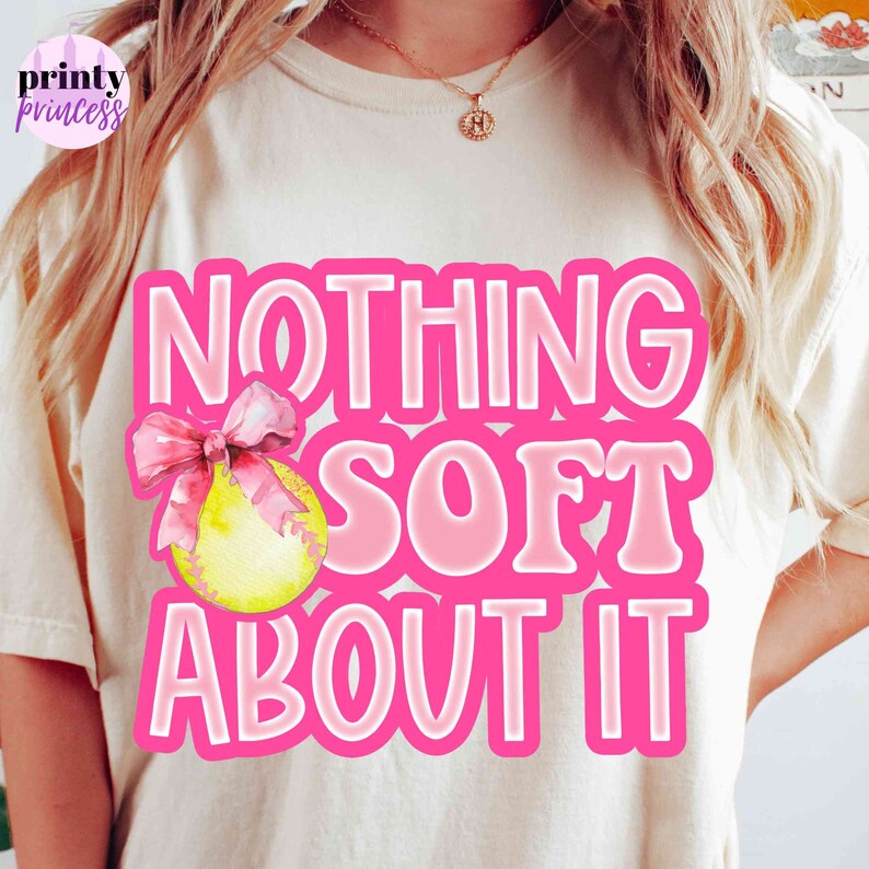 May include: A white t-shirt with a pink graphic that says "NOTHING SOFT ABOUT IT" with a pink ribbon and a yellow softball.