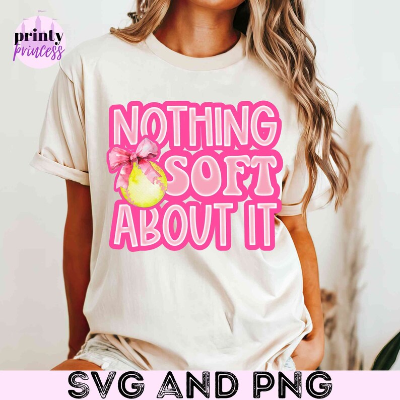 May include: A white t-shirt with a pink graphic that says "Nothing Soft About It" with a pink bow and a yellow softball.