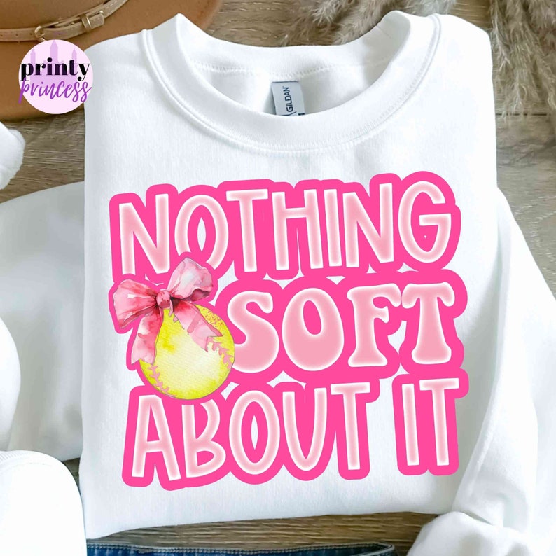 May include: White sweatshirt with pink lettering that says "Nothing Soft About It" with a pink bow and yellow softball graphic.