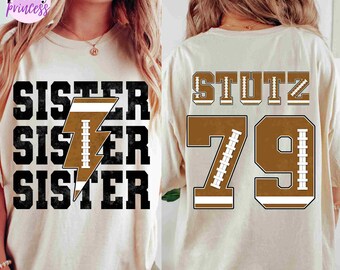 May include: Two white t-shirts with a football theme. The front shirt has the word "Sister" repeated three times with a brown football lightning bolt graphic. The back shirt has the name "Stutz" and the number "79" in brown with white football laces.