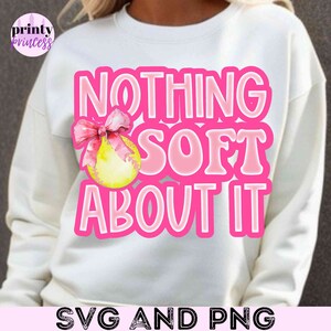May include: White sweatshirt with pink text that reads "Nothing Soft About It" and a pink bow with a yellow softball graphic.