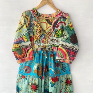 以下が含まれることがあります： Vネックと花柄のカラフルなマルチレイヤーロングスリーブドレス。パッチワークデザインで、異なる生地とパターンが使用されています。ウエストは紐で結ばれています。