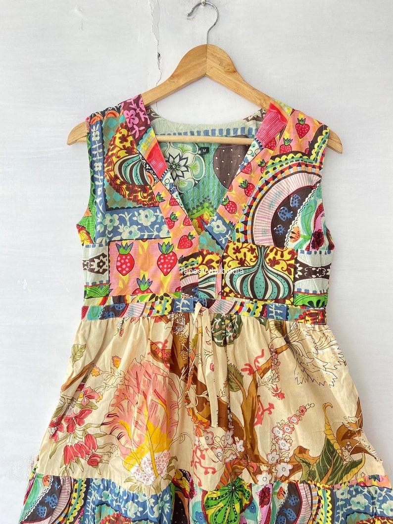 Op de afbeelding: Een mouwloze jurk met een patchwork-ontwerp met een verscheidenheid aan kleurrijke patronen, waaronder bloemen, geometrische en abstracte motieven. De jurk heeft een V-hals en een strik in de taille.