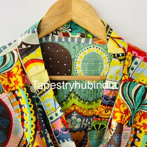 May include: A colorful fabric with a patchwork design featuring circles, flowers, and geometric patterns in shades of yellow, red, blue, green, and brown. The fabric is hanging on a wooden hanger. The text "Tapestryhubindia" is visible in the center of the image.