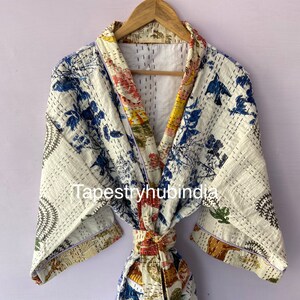 Può includere: Accappatoio bianco in cotone con stampa floreale e cintura annodata. L'accappatoio ha un motivo floreale blu e bianco con un motivo floreale giallo e rosso all'interno. L'accappatoio è trapuntato e ha un bordo blu chiaro.