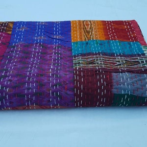 Pode incluir: Uma colcha de retalhos colorida feita de saris reciclados. A colcha está dobrada ao meio e tem uma variedade de cores, incluindo roxo, azul, vermelho, laranja e verde.