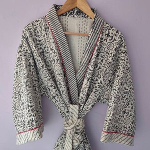 May include: A white robe with a black and white patterned design. The robe has a red trim and a tie belt.