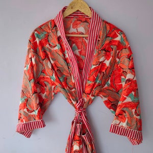 Op de afbeelding: Een rood-witte badjas met een bloemenprint. De badjas heeft lange mouwen en een strikceintuur.