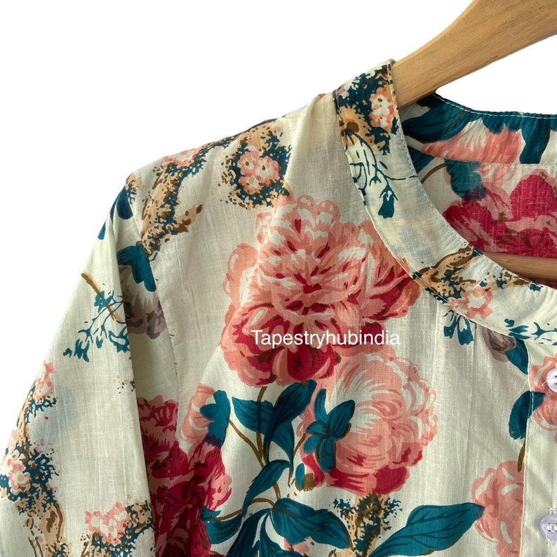 May include: A white cotton shirt with a floral print featuring pink, red, and teal flowers. The shirt has a mandarin collar and a button closure. The text "Tapestryhubindia" is visible on the shirt.